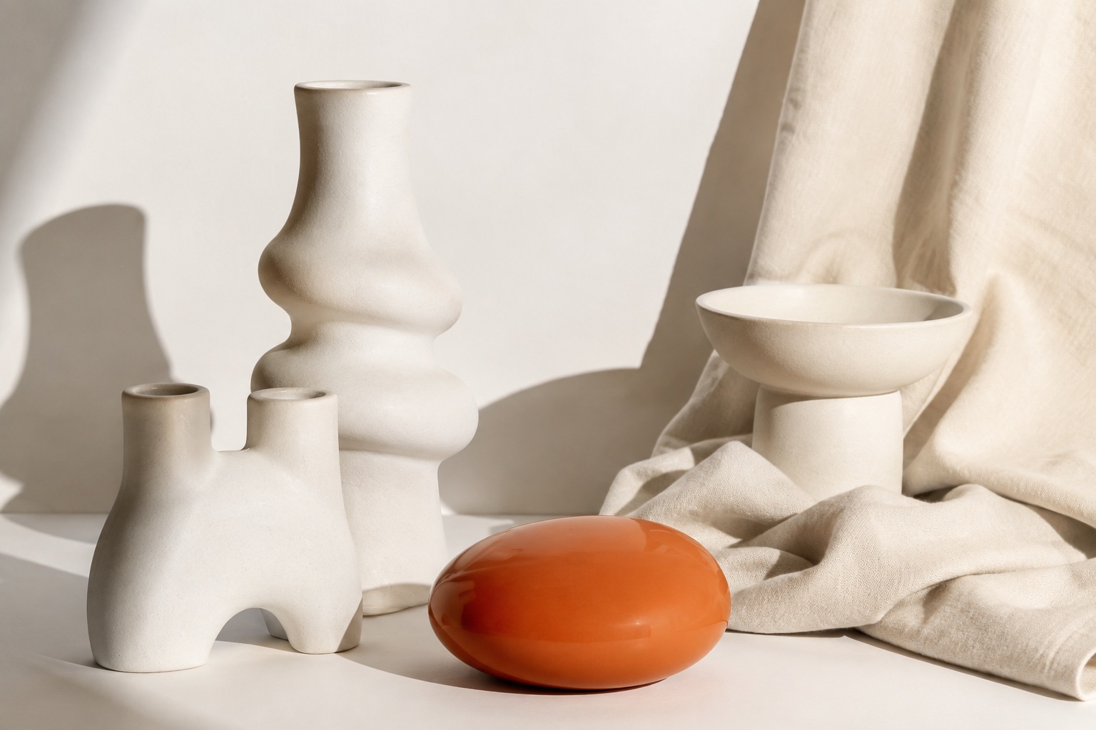 Pale sculptural ceramics and orange glass on cream fabric.