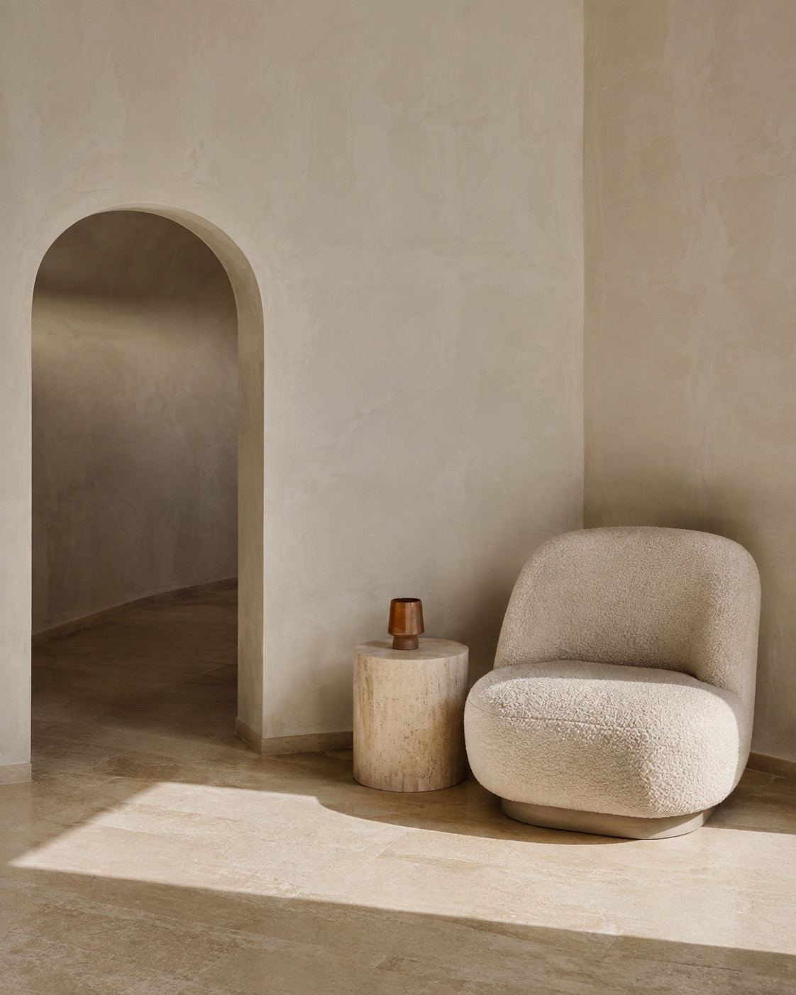 A sculptural armchair beside an arched doorway and sunlit plaster wall.