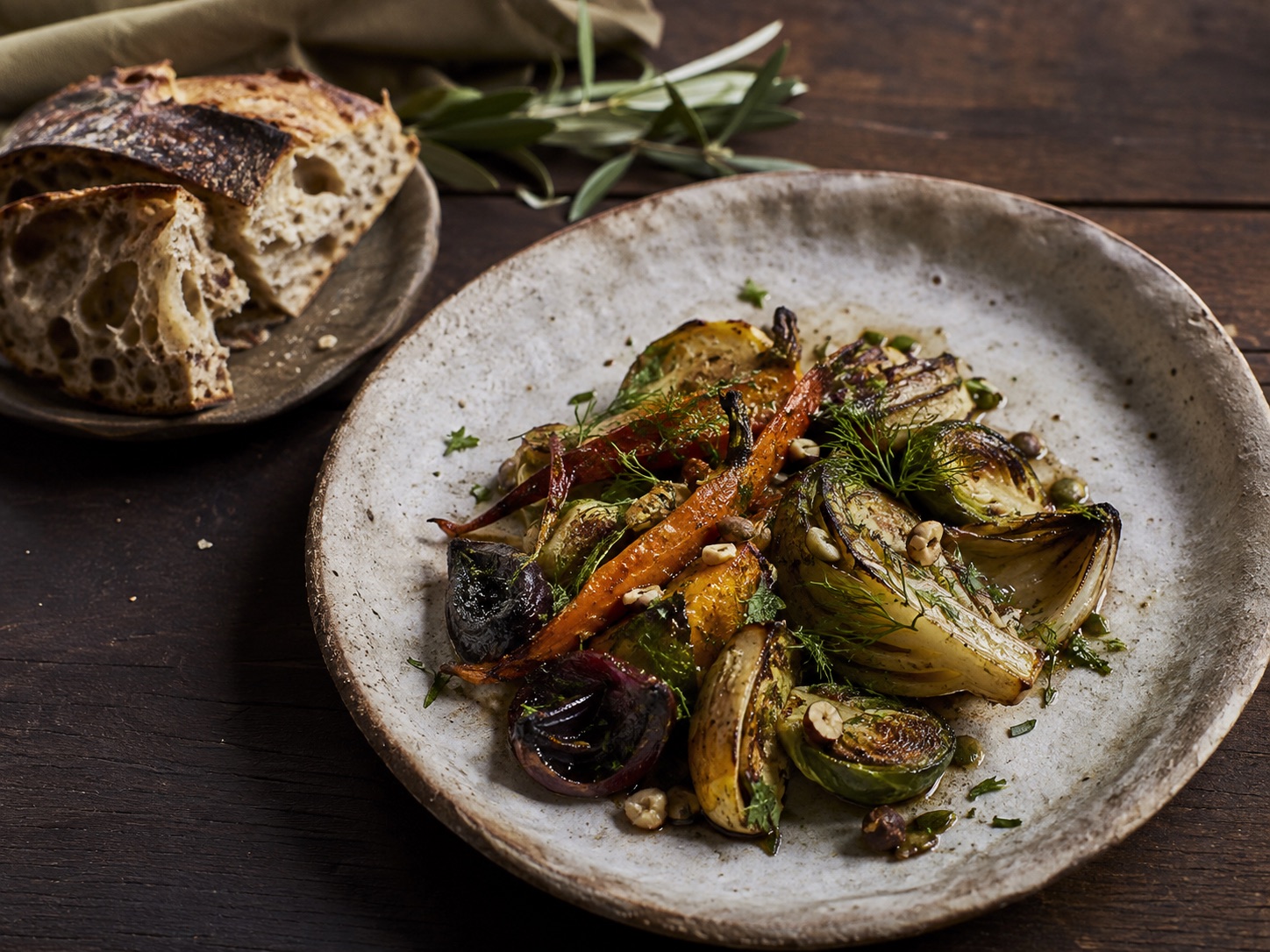 An illustrative seasonal plate of roasted vegetables and herbs beside sourdough